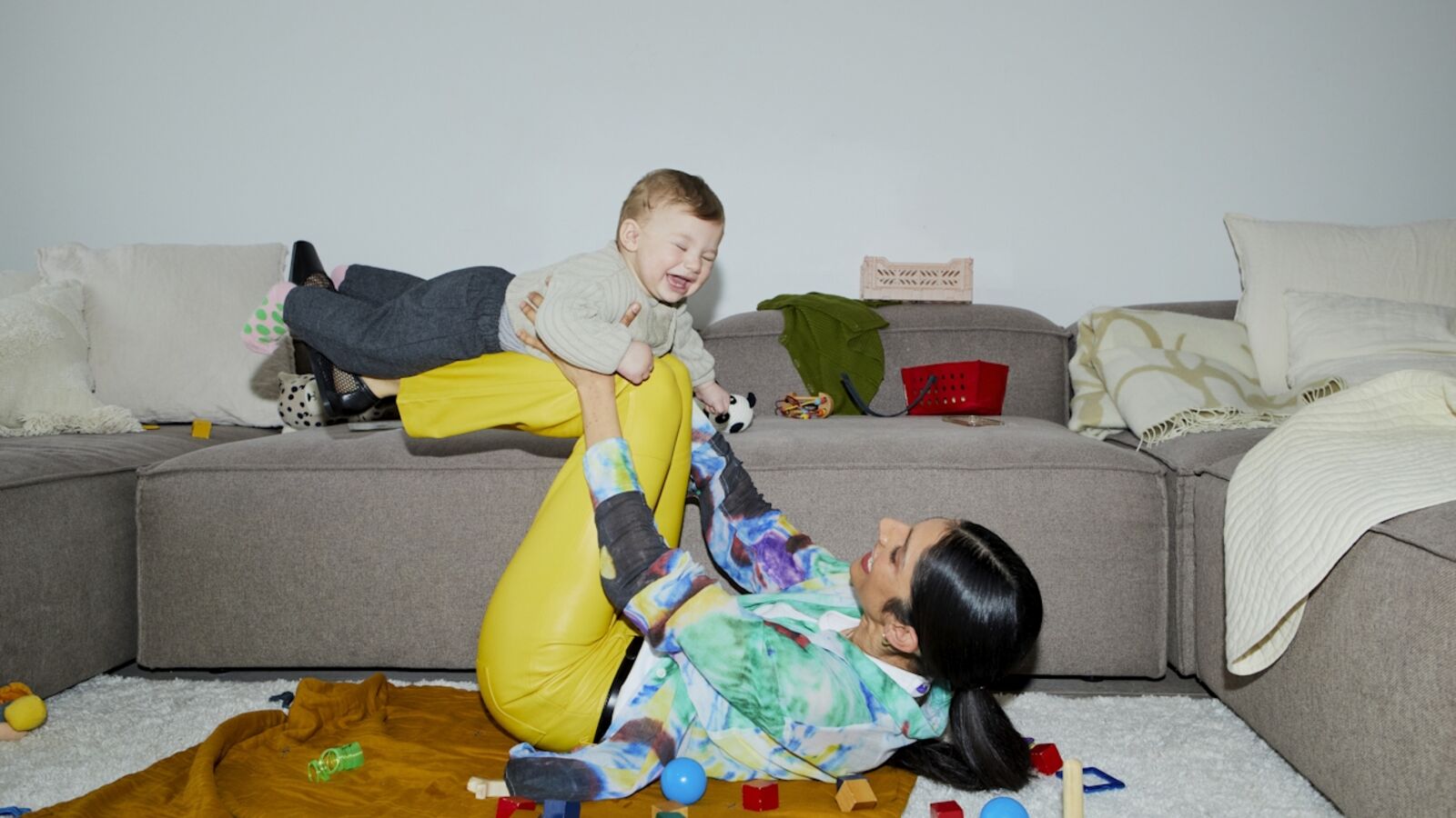 Mutter liegt auf dem Boden und spielt mit Baby, das sie hochhebt